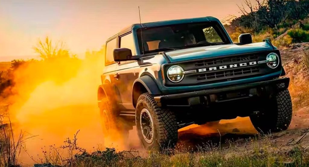 An image of a blue 2024 Ford Bronco tearing over a hill in the sunset, leaving a cloud of dust behind. 